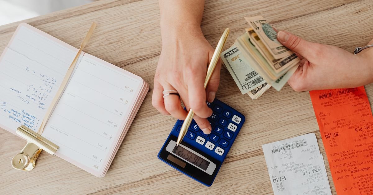 Hands organizing cash, receipts, and a calculator on a table