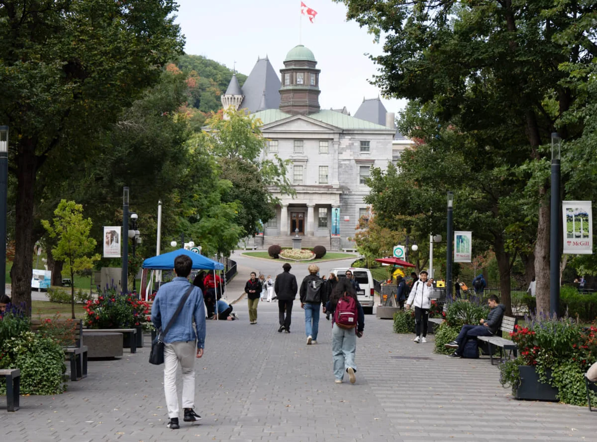Students walking a tree-lined path toward a historic university campus building
