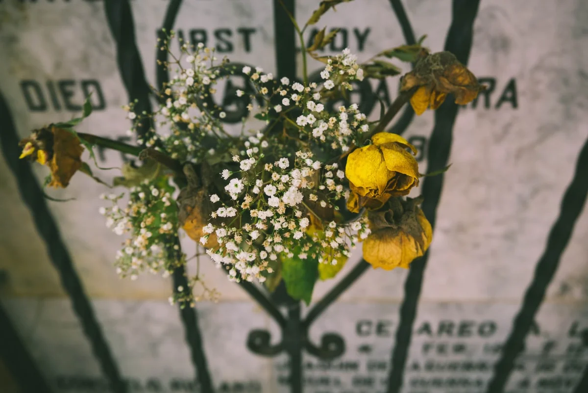 Wilted flowers in an iron holder before a weathered gravestone