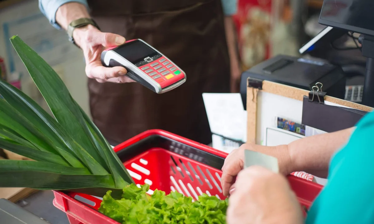 Hand tapping a payment terminal at a grocery checkout