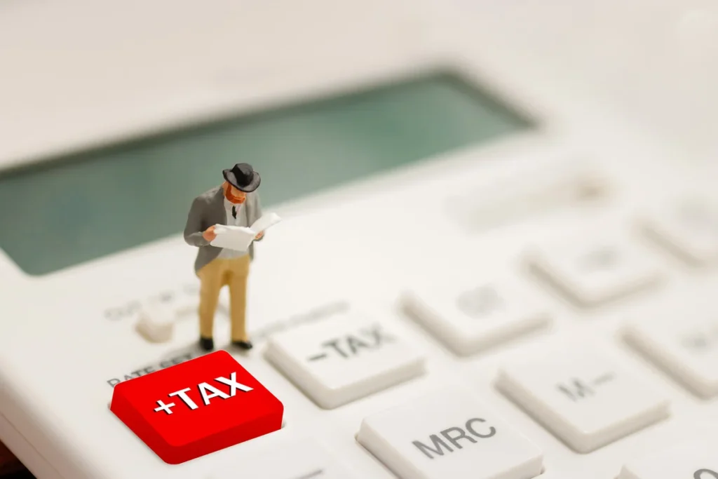 Miniature businessman on calculator reviewing taxes, kitchen-table finance theme