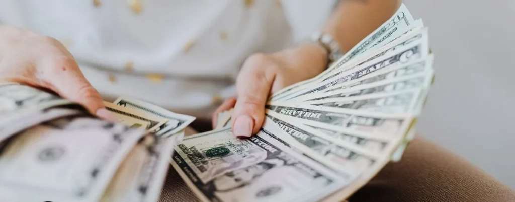 Hands fanning stacks of US dollar bills on a lap