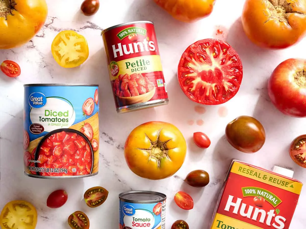 Canned tomatoes and fresh tomatoes on marble countertop