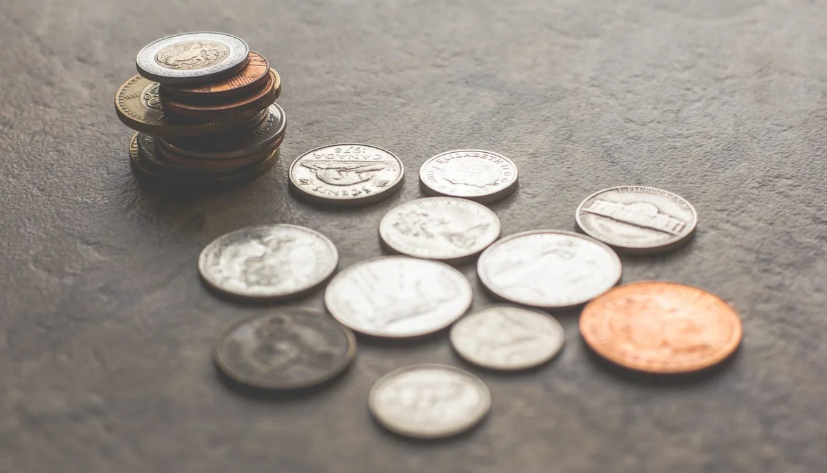 Stack and scattered pile of coins on a dark surface